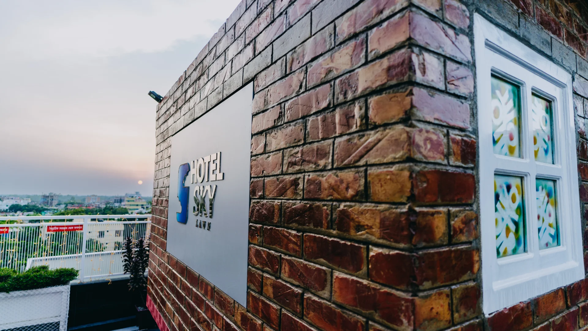 Hotel Sky Lawn’s rooftop terrace area features a textured brick wall with a bold "Hotel Sky Lawn"...
