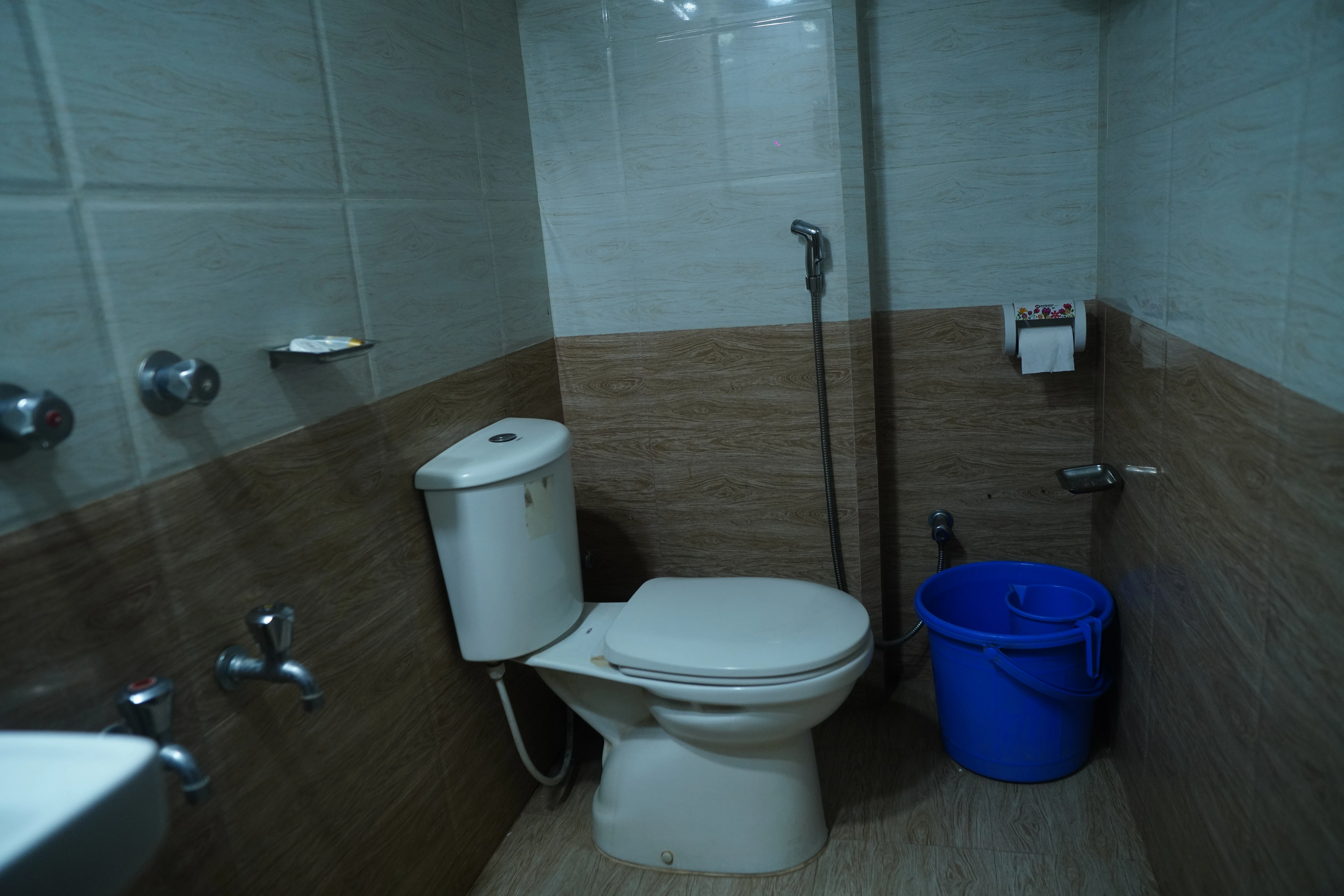 Sky Lawn Hotel’s accessible bathroom features a white toilet, sink fixtures, a blue bucket, and a...